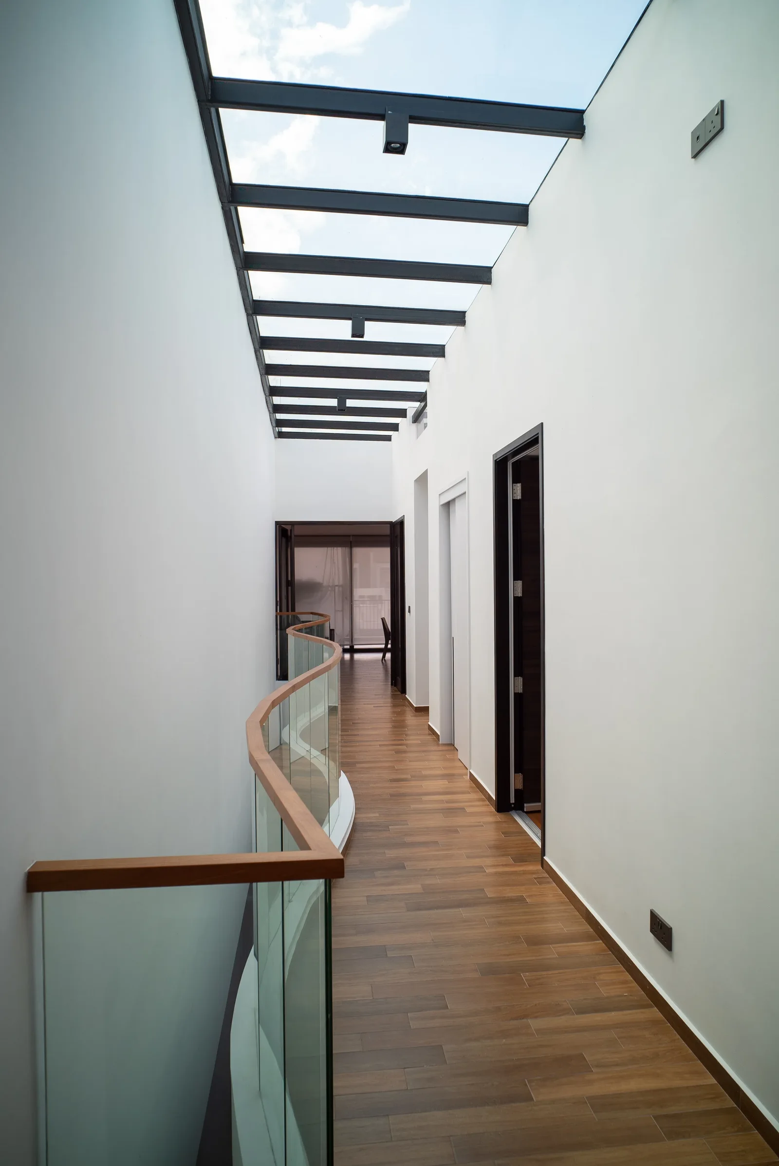 J Concept Designers &mdash; upper floor skylit corridor with curved timber-topped glass balustrade